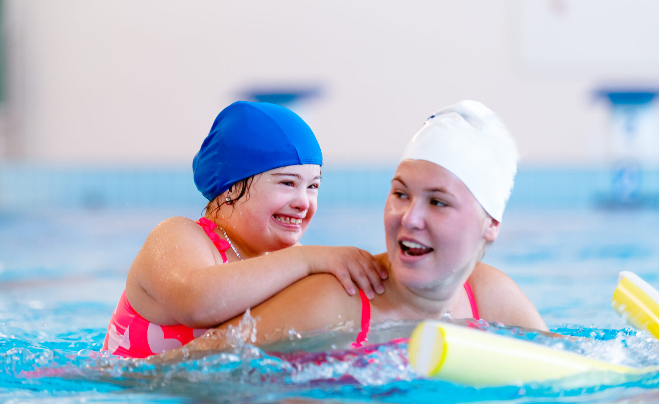 Photo of young girl with Down Syndrome and autism happily participating in a private swimming lesson with a female swim teacher.